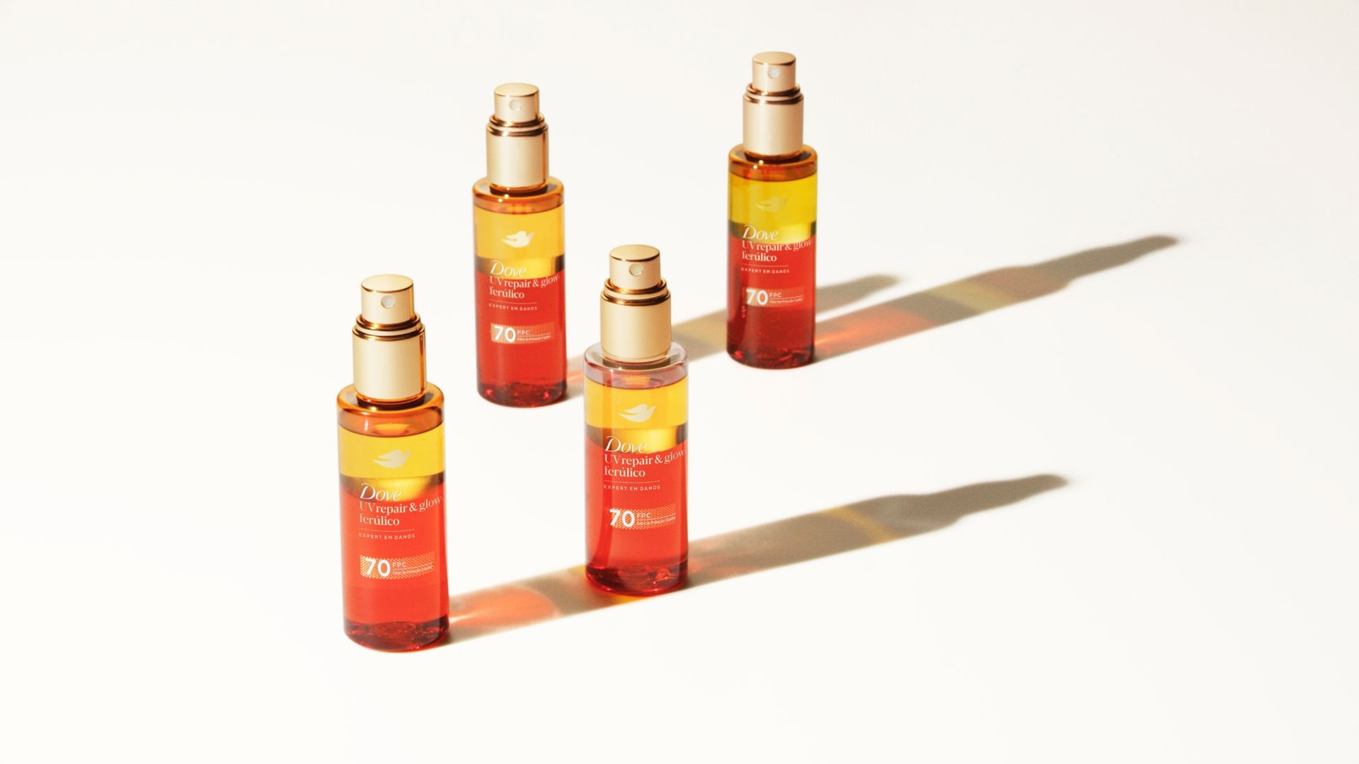Quatro frascos do sérum bifásico UV Repair & Glow da Dove, para proteger o cabelo dos danos causados pelos raios UV. Frascos de vidro com sérum laranja e amarelo.
