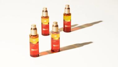 Quatro frascos do sérum bifásico UV Repair & Glow da Dove, para proteger o cabelo dos danos causados pelos raios UV. Frascos de vidro com sérum laranja e amarelo.