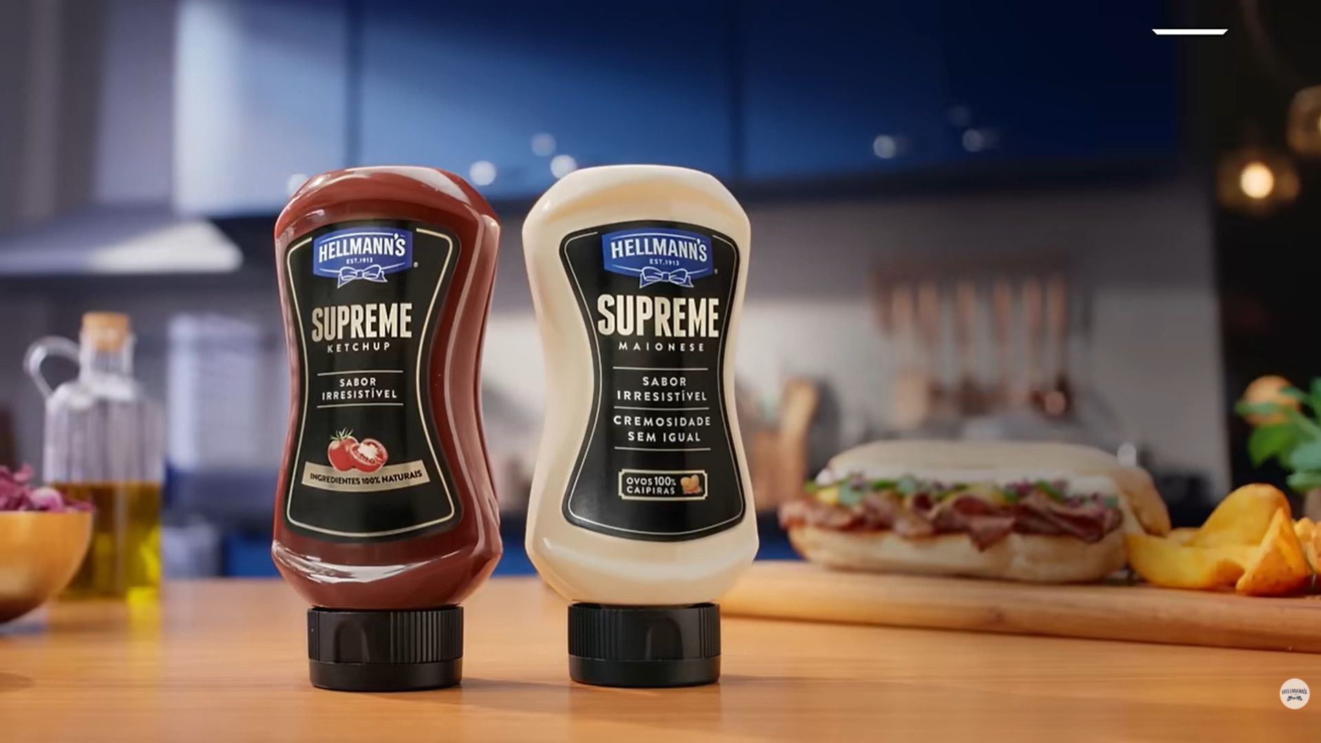 Duas garrafas de ketchup e maionese Hellmann's Supreme sobre a bancada da cozinha, com um sanduíche e batatas fritas ao fundo.