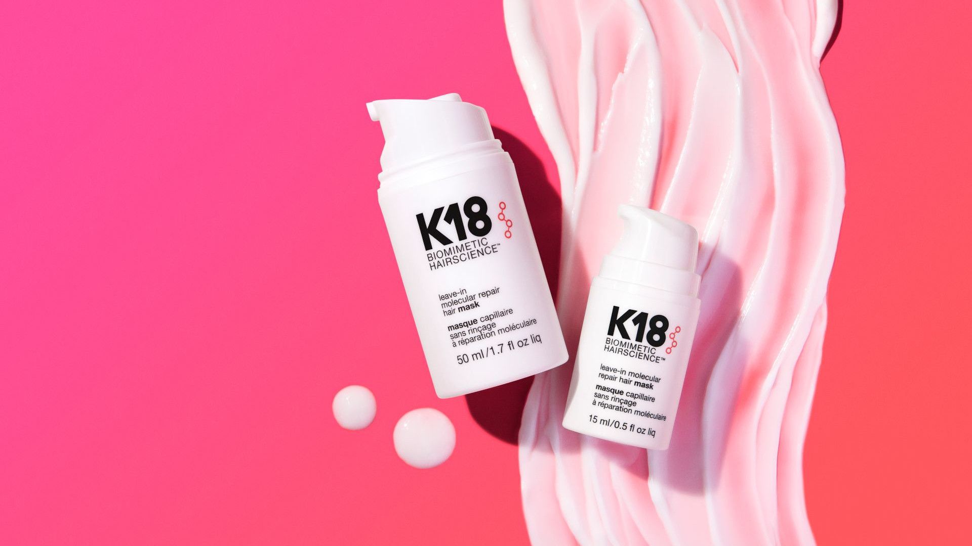 Dois frascos brancos de tratamento capilar K18 colocadas sobre um fundo rosa com creme em espiral.