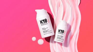 Dois frascos brancos de tratamento capilar K18 colocadas sobre um fundo rosa com creme em espiral.