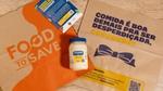 Uma mesa de madeira clara comporta duas sacolas recicláveis: Uma sacola de papel kraft com o logo laranja escrito "Food To Save" , ao meio um pote de maionese Hellmann's com outra sacola em papel kraft com o logo de Hellmann's e a frase "Comida é boa demais para ser desperdiçada, concorda?"