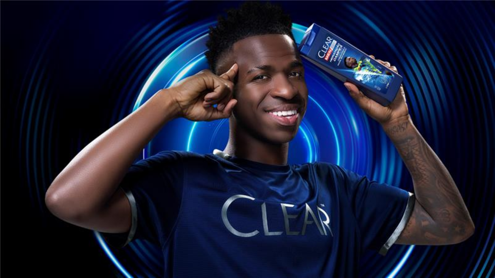 Um homem com uma camisa azul escura com o logotipo da Clear segura um frasco de champô Clear.