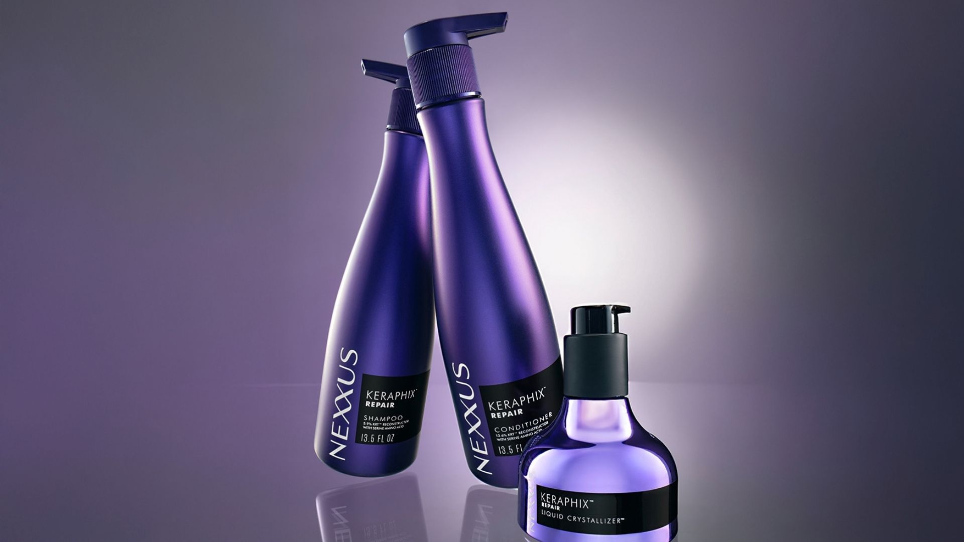 Três frascos de produtos Nexxus Keraphix. Frascos lilás de shampoo e condicionador, e um frasco metálico menor com dosador preto.