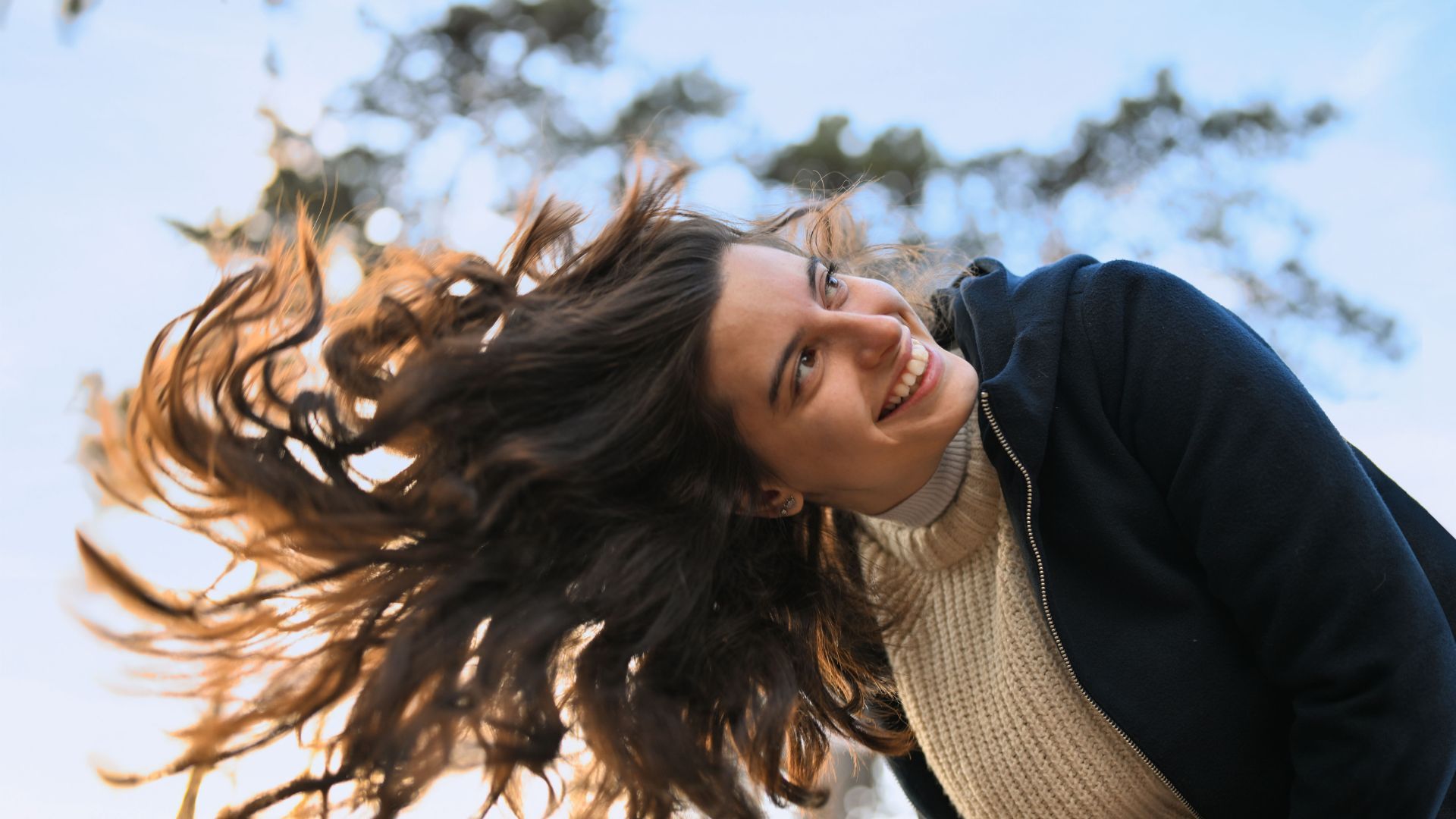 Jovem sorridente ao ar livre balançando o cabelo comprido contra um céu limpo.