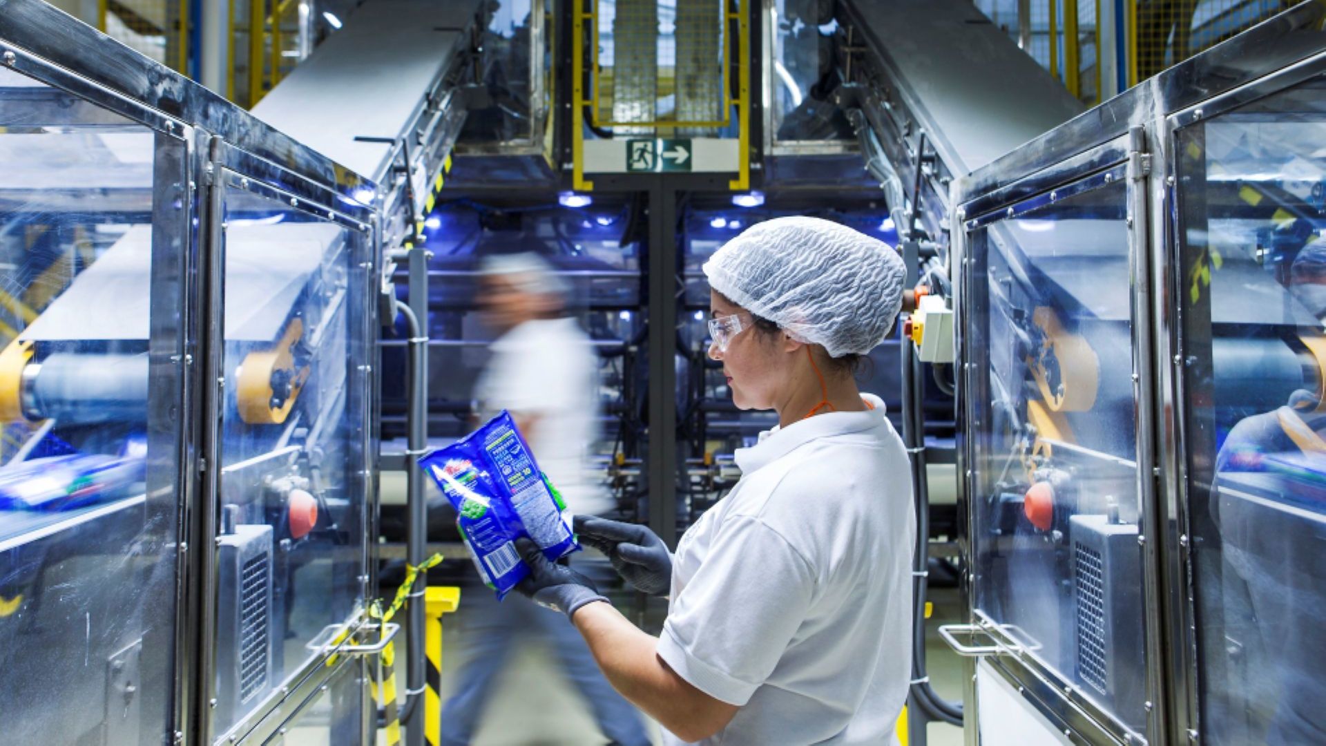 Um operário de fábrica com touca e uniforme brancos observando uma embalagem.